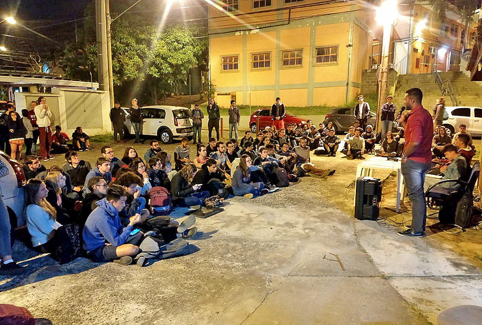 foto mostra matheus em frente a plateia de alunos sentados no chão e ele falando com eles em pé