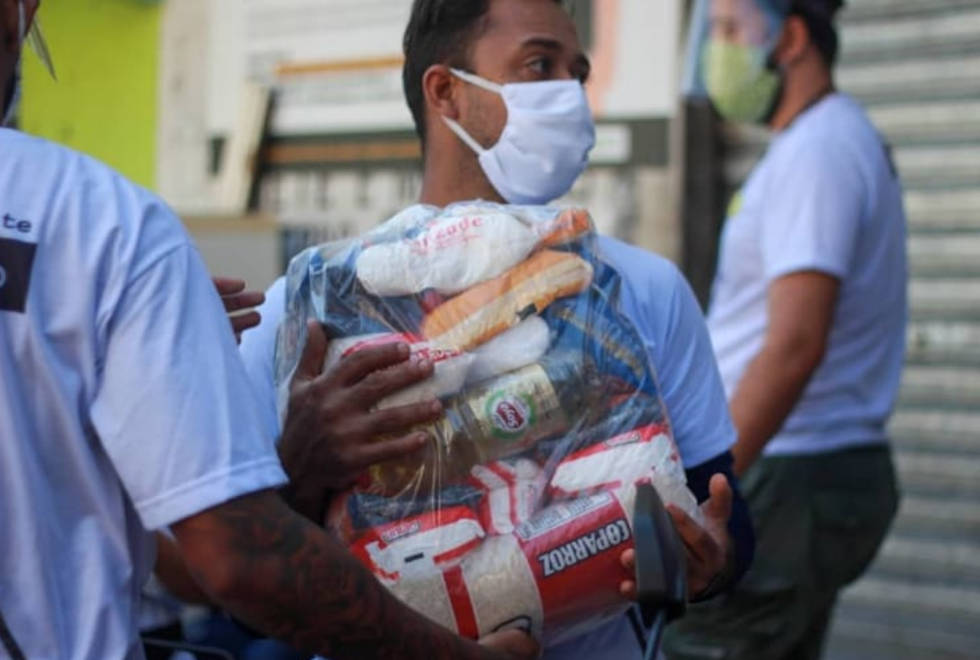 foto mostra pessoa vestindo máscara carregando uma cesta básica