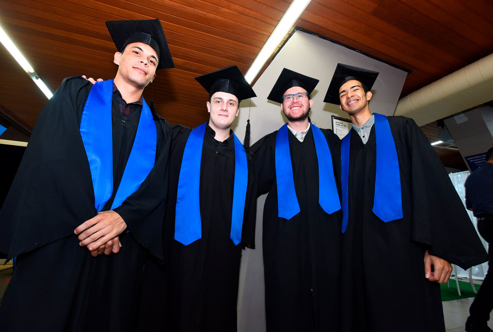 foto mostra quatro alunos do profis, todos rapazes, posando para foto. eles vestem becas e capelos