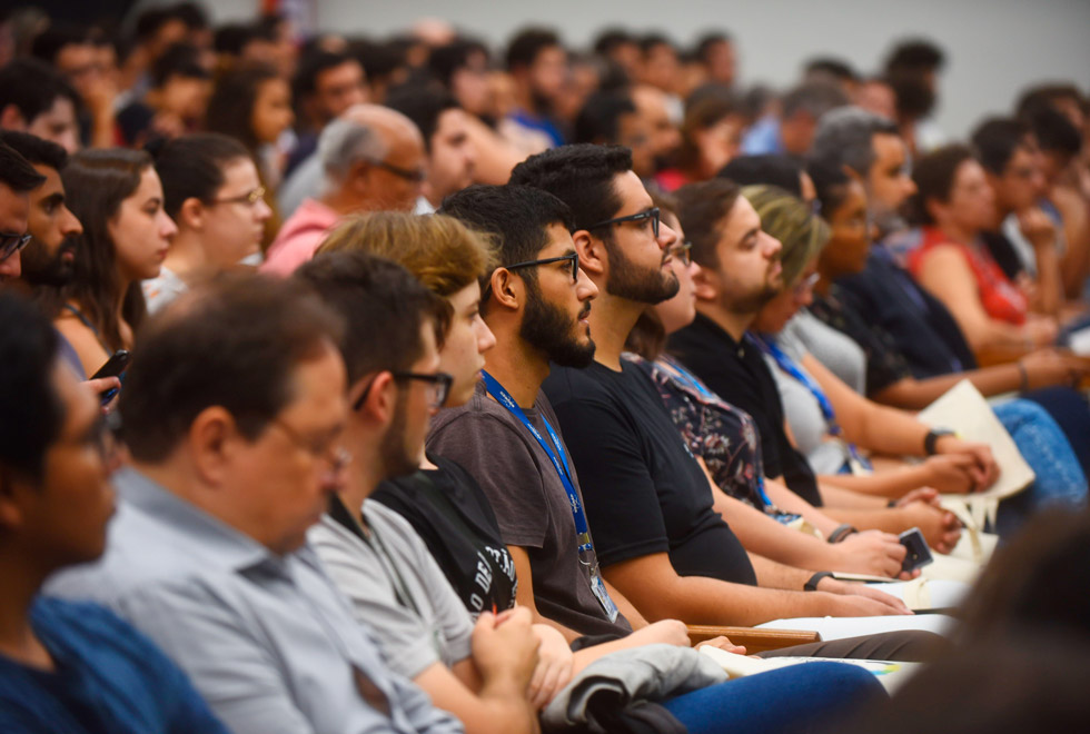 audiodescrição: fotografia colorida foca na plateia que assiste à palestra no centro de convenções