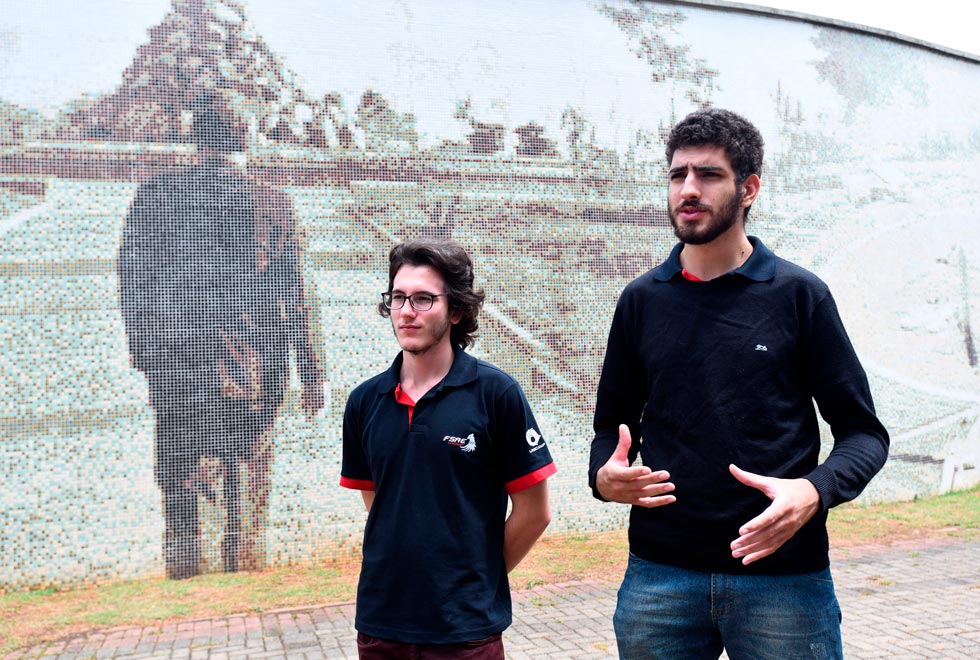 foto mostra vinicius vieira e renan garcia em frente ao mural de zeferino vaz, na praça das bandeiras do campus da unicamp