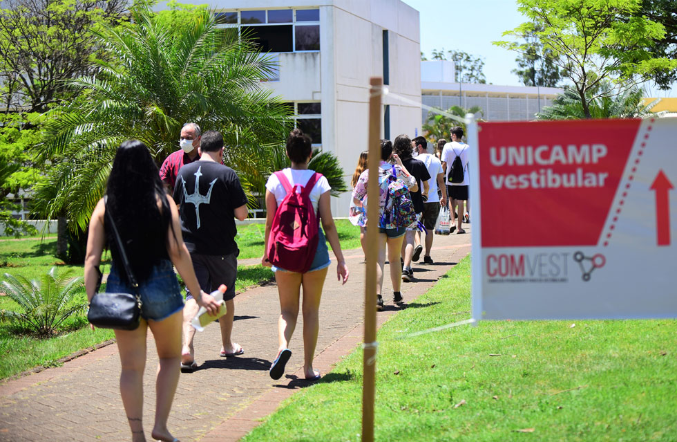 audiodescrição: fotografia colorida de estudantes caminhando; no primeiro plano há uma placa escrito "vestibular unicamp"