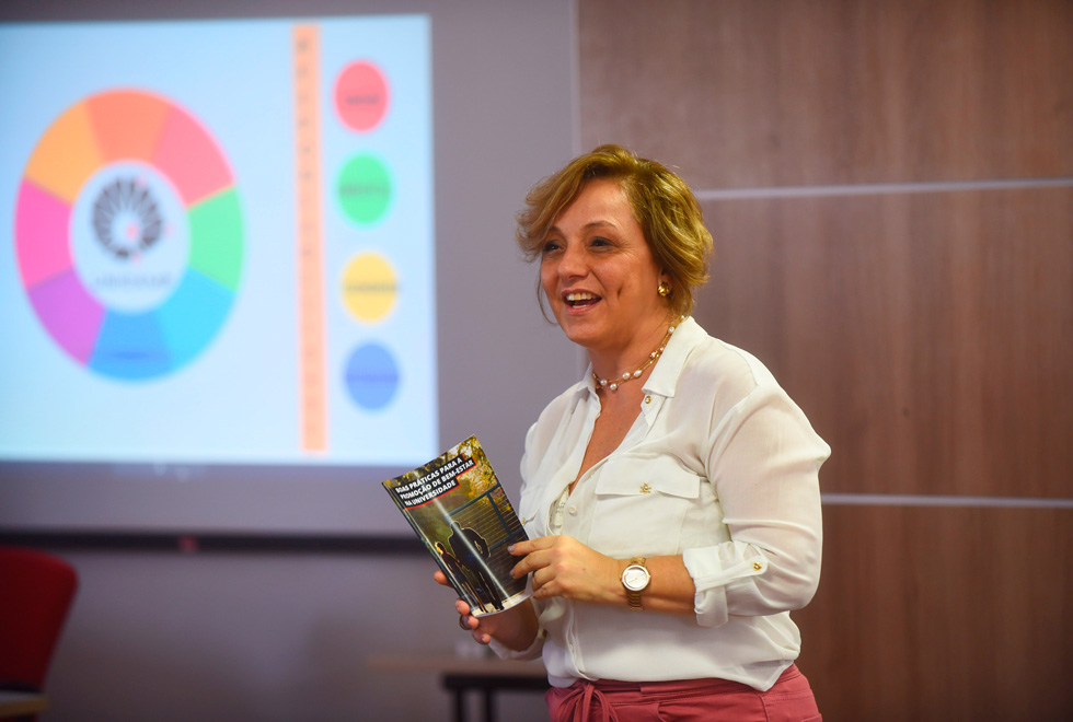 foto mostra professora eliana amaral em uma apresentação segurando uma cartilha sobre bem estar na universidade
