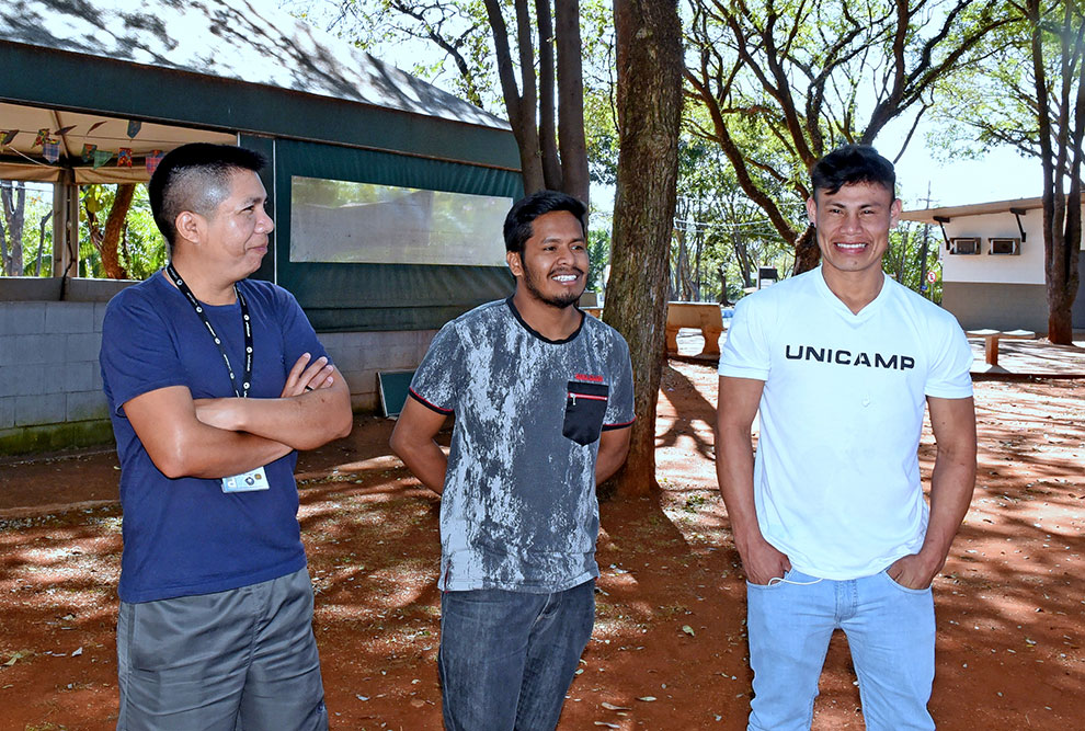 Foto mostra três estudantes indígenas em pé em uma praça. Eles estavam dando entrevista e sorriem