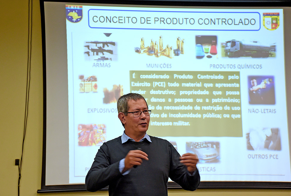 Samuel Sidney está falando para os estudantes sobre os produtos controlados, expostos em um slide que está iluminado no telão atrás do militar