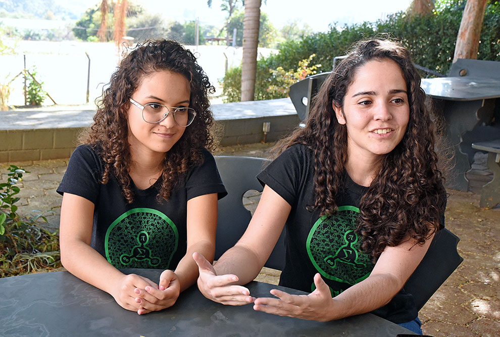 Na foto aparecem Renata à esquerda e Monique à direita, sentadas, com a camiseta do curso