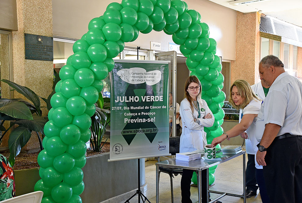 Bexigas e cartazes aparecem no espaço da campanha Julho Verde. No cartaz está escriti "julho verde, 27/07 dia mundial do câncer de cabeça e pescoço, previna-se"