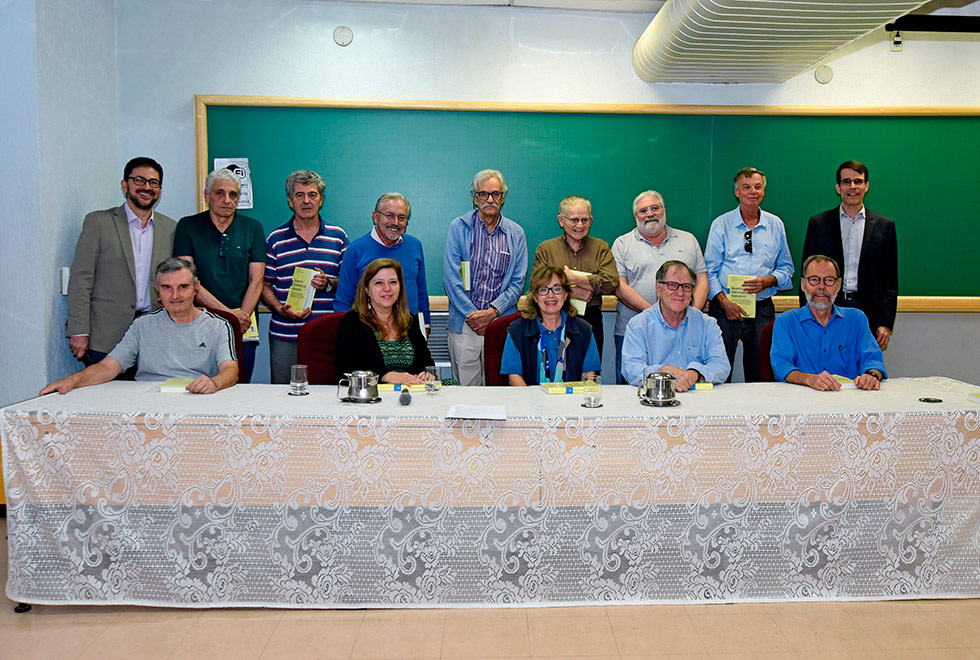 Todos os autores do livro posam para a foto, alguns estão sentados atrás da mesa, outros de pé