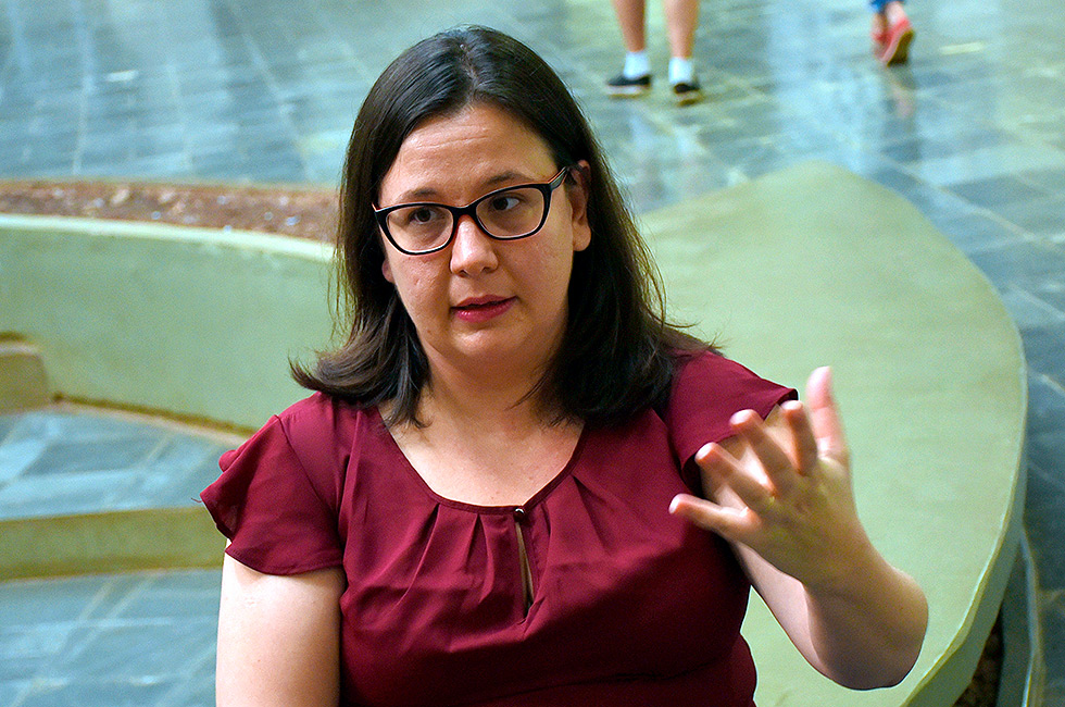 Professora Anne, com blusa vermelha, um dos braços levantados, gesticulando durante entrevista no saguão do Imecc