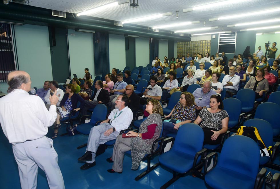 Publico presente no salão nobre da Faculdade de Ciências Médicas acompanha a palestra de Naomar de Almeida. Na foto, o publico está a direita, olhando para a apresentação de slides com o professor Naomar a esquerda. 