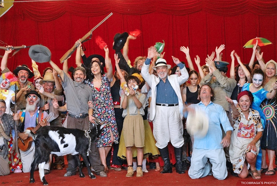 Toda a equipe do filme, inclusive o ator Lima Duarte, posam para a foto sorridentes, sobre um palco e com uma cabra