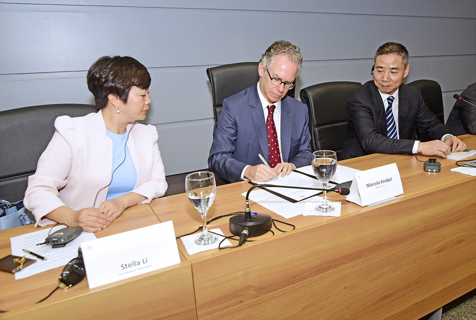 Marcelo Knobel assina documento de cooperação, observado por representantes da empresa chinesa