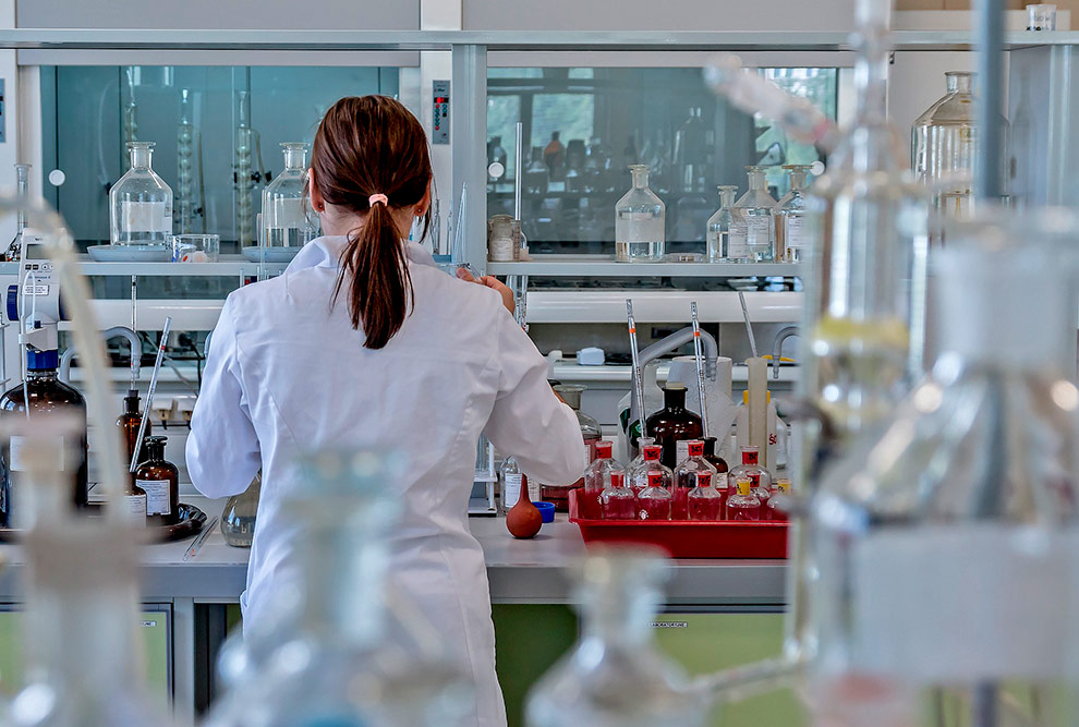 Foto de uma mulher que aparece de costas, de pé, em um laboratório de ciências.