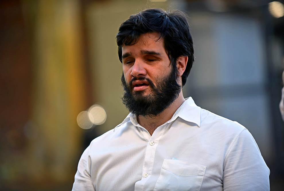 Foto de um homem que aparece do peito para cima. Ele é branco, tem o cabelo e a barba pretos e usa uma camisa branca.