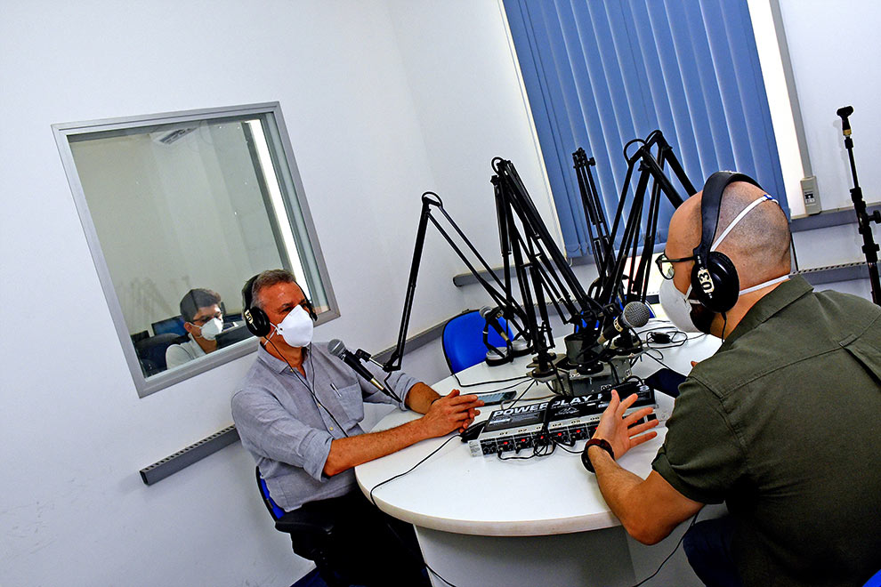 foto mostra reitor tom zé no estúdio da rádio falando ao microfone. ele usa máscara