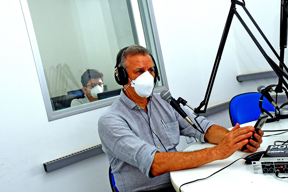 foto mostra reitor tom zé no estúdio da rádio falando ao microfone. ele usa máscara