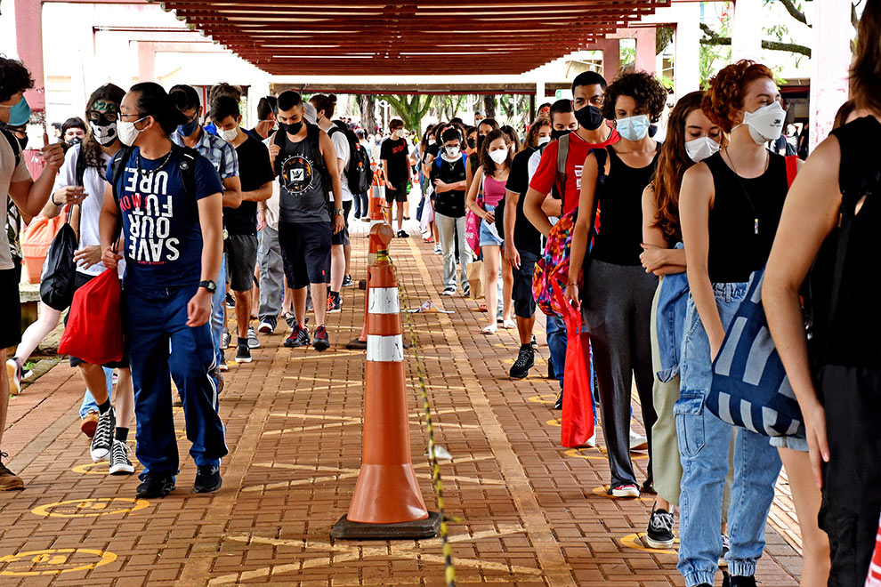 foto mostra estudantes em fila para entrar no restaurante universitário da unicamp. todos usam máscara