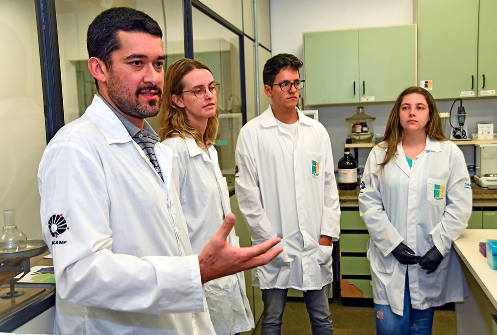 audiodescrição: fotografia colorida mostra quatro pessoas de jaleco branco dentro de um laboratório de pesquisa