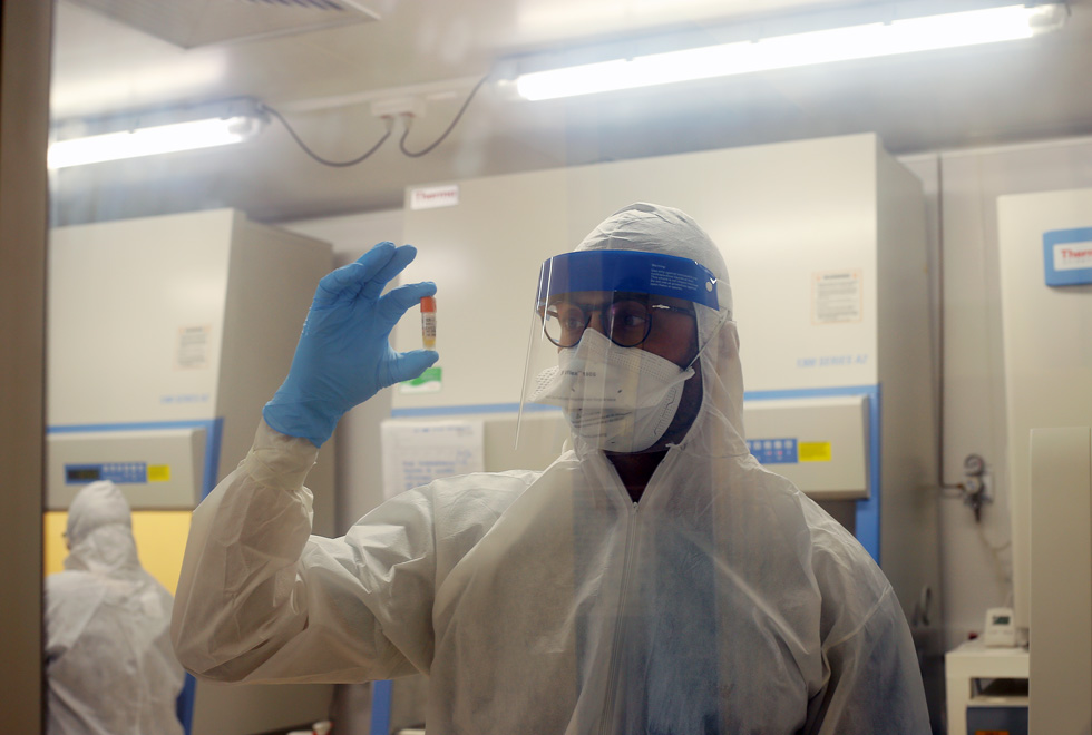 audiodescrição: fotografia colorida mostra pesquisador com frasco do coronavírus dentro do laboratório