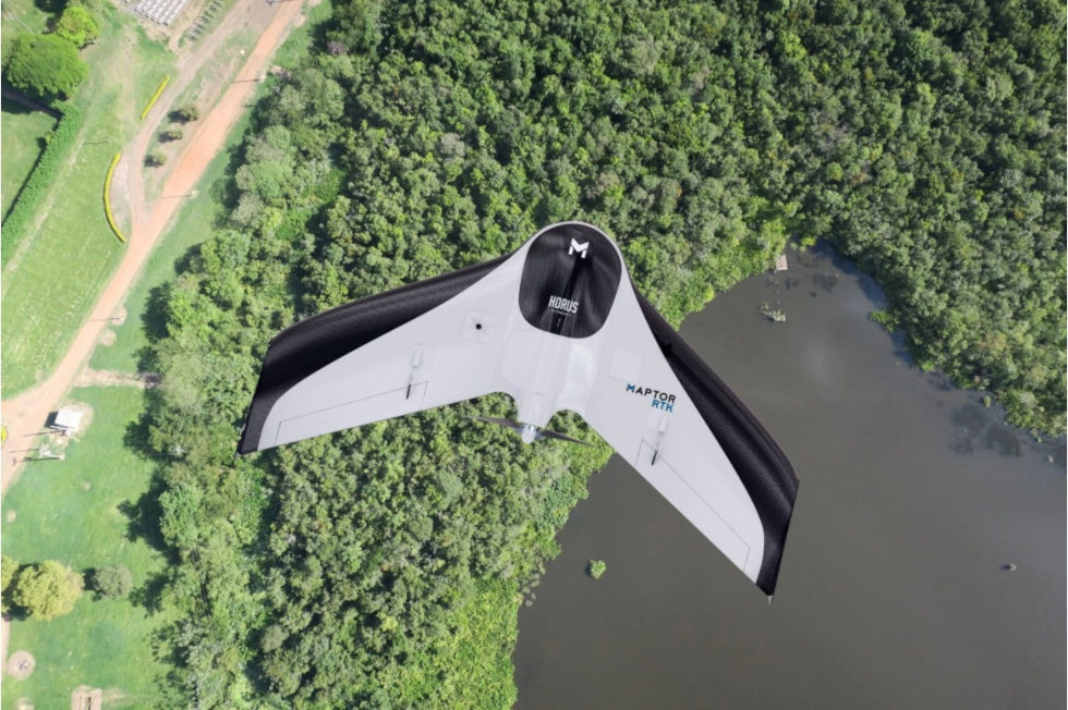 foto mostra drone de asas fixas sobrevoando uma área rural