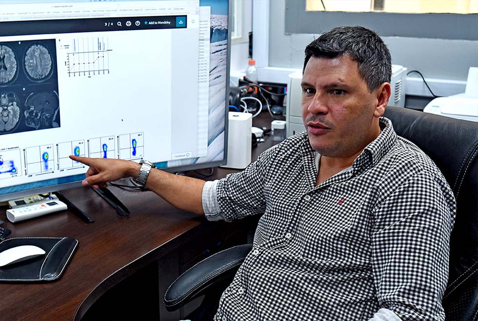 foto mostra professor alessandro farias sentado apontando o dedo para a tela de um computador