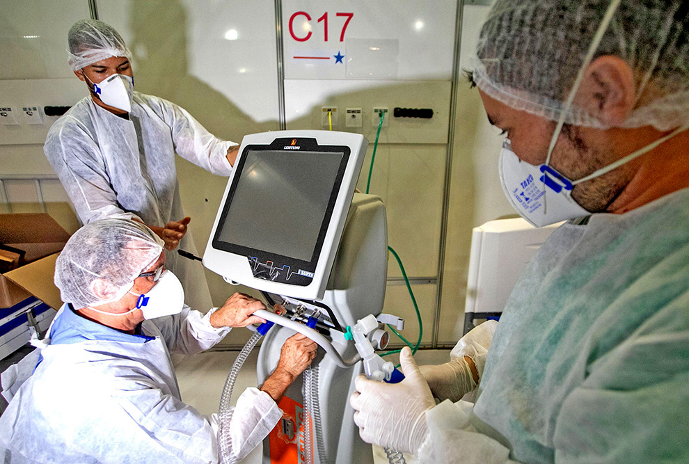 foto mostra profissionais de saúde, vestindo roupas de segurança, instalando um respirador artificial