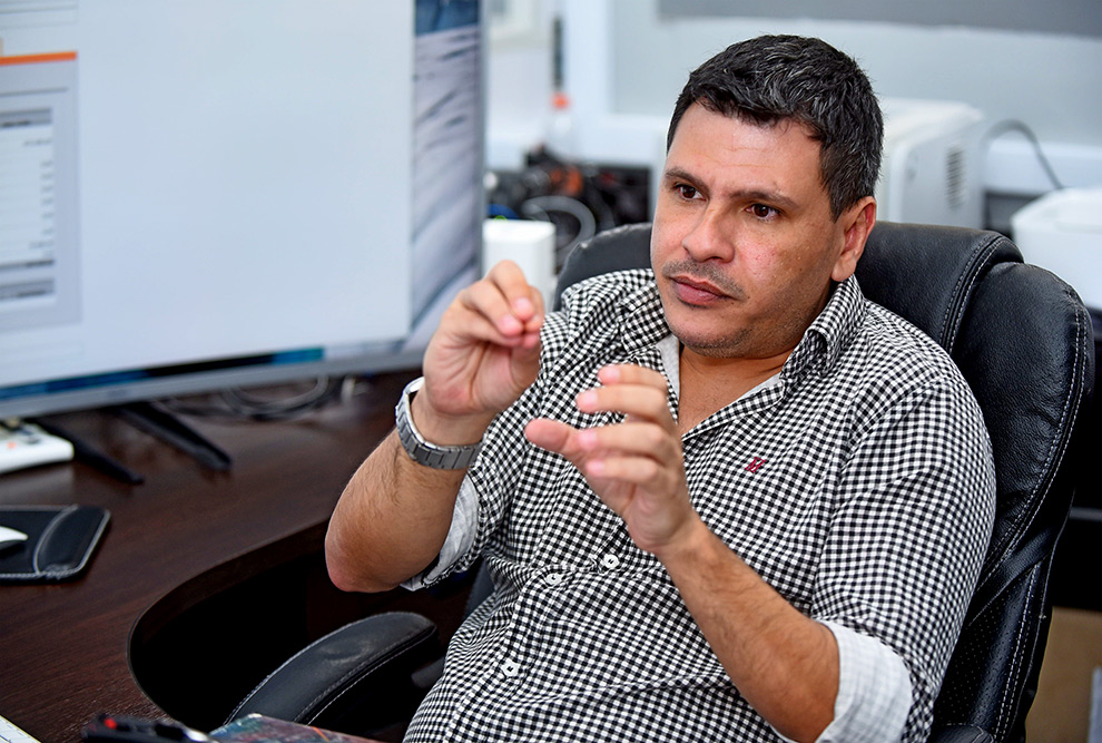 foto mostra o professor alessandro farias sentado em uma cadeira de escritório gesticulando enquanto fala