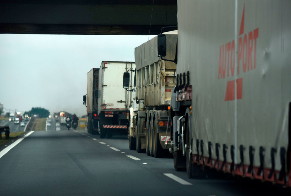 foto mostra traseiras de caminhões em uma rodovia