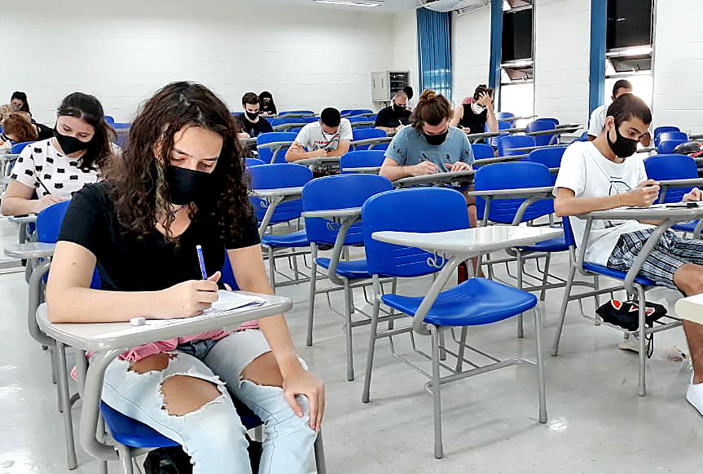 audiodescrição: fotografia colorida de uma sala de aula com estudantes realizando provas
