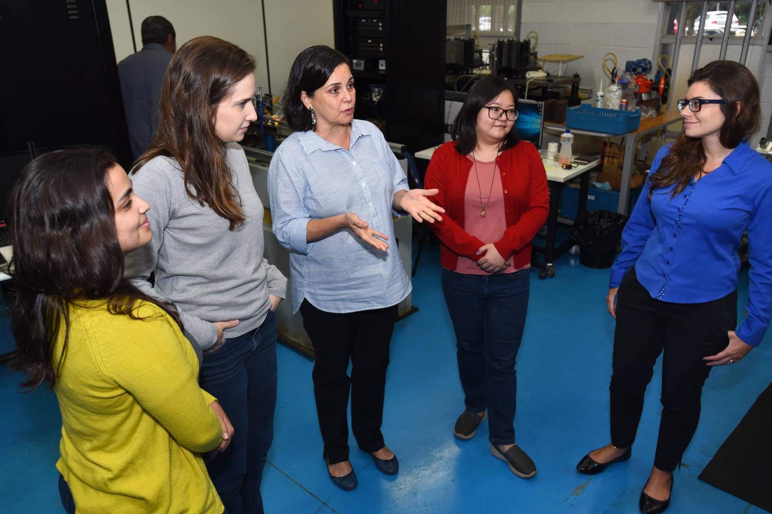 audiosdescrição: fotografia colorida mostra professora Kátia, em laboratório, junto a quatro alunas da pós-graduação, elas estão em pé na sala