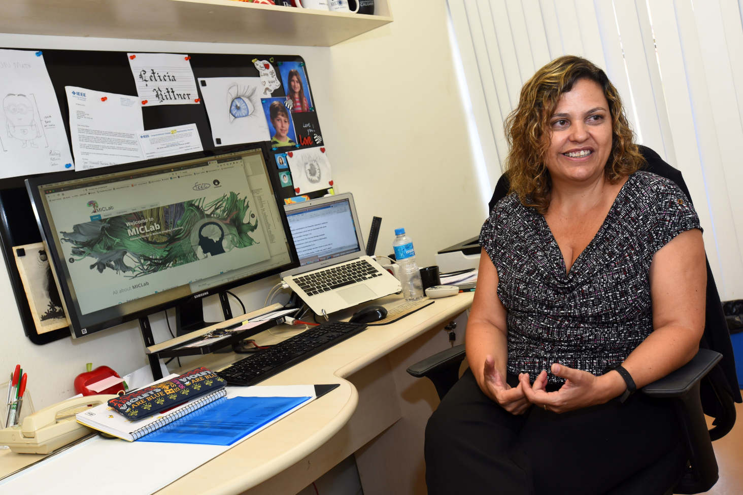 audiodescrição: fotografia colorida mostra professora Leticia sentada em frente ao computador durante uma entrevista