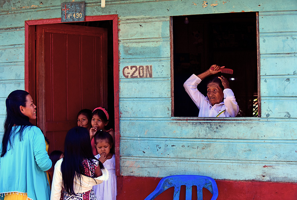 audiodescrição: fotografia colorida de casa azul onde estão moradoras da comunidade umariaçu na janela e em frente à porta