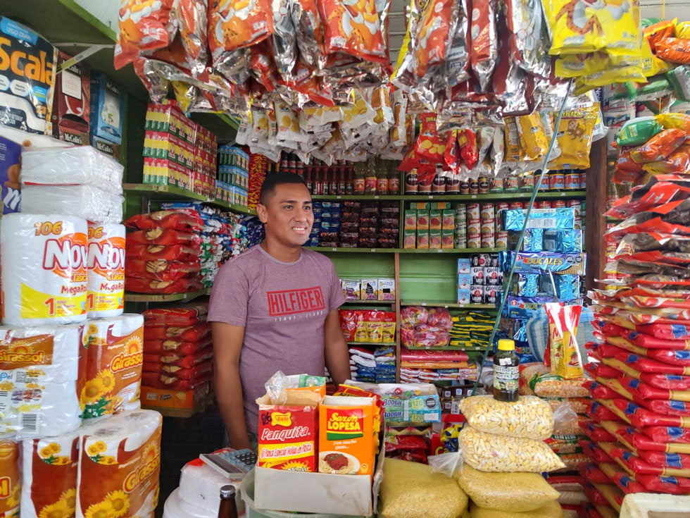 audiodescrição: imagem colorida, em sua loja, produtos ao fundo, comerciante peruano Kayan Caballero no centro da imagem. (Foto: Antonio Scarpinetti)