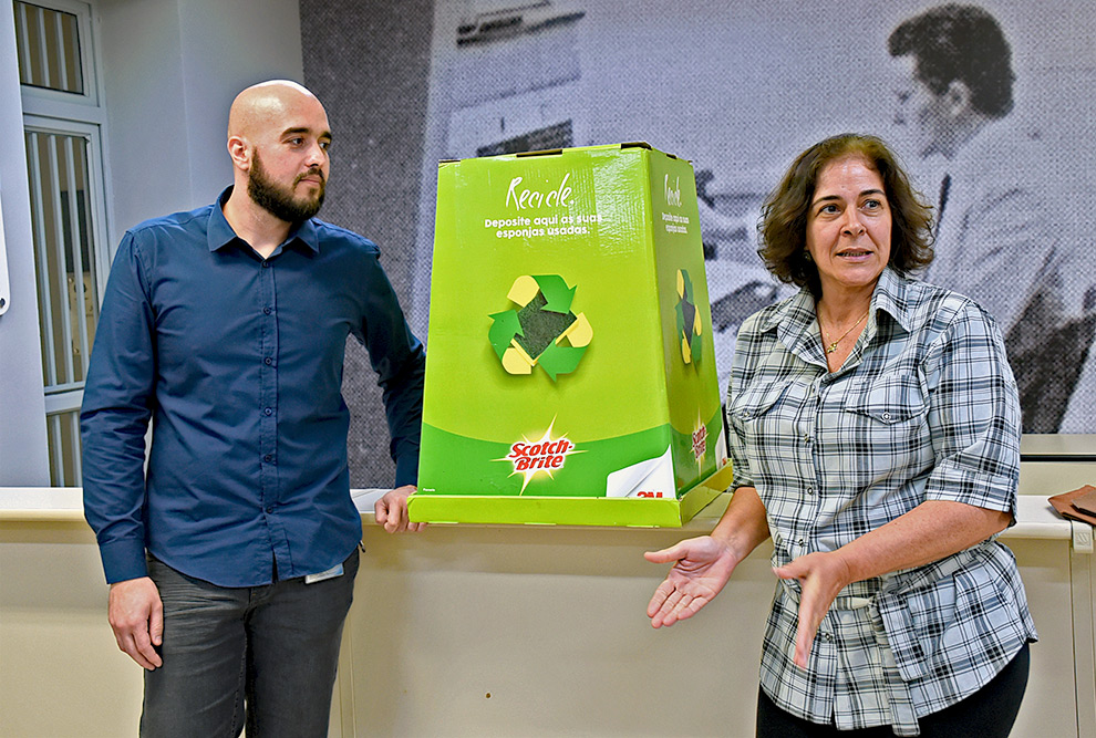 Os funcionários Paulo e Rosângela aparecem junto a caixa coletora de esponjas para reciclagem