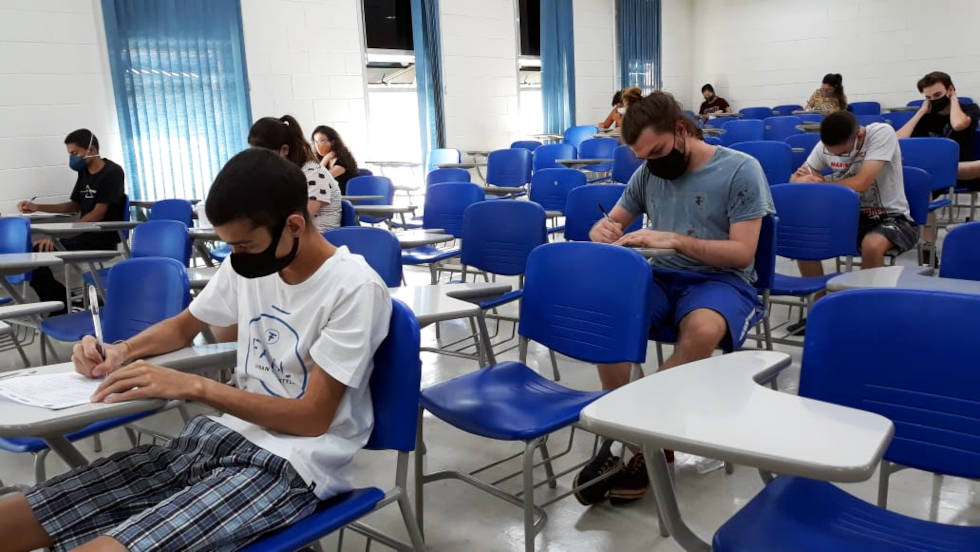 audiodescrição: fotografia colorida mostra estudantes fazendo prova de vestibular; eles estão de máscaras, as carteiras são azuis e há poucos candidatos na sala, conforme protocolos de distanciamento social