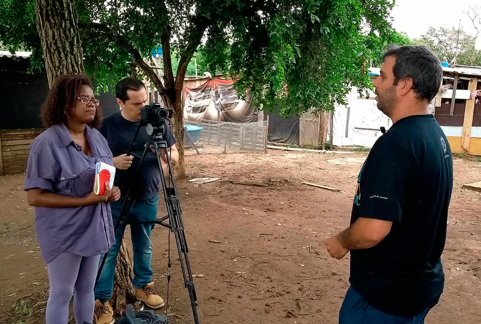 Repórter e cinegrafista aparecem de frente e entrevistado de costa nesta imagem de bastidor da produção do documentário