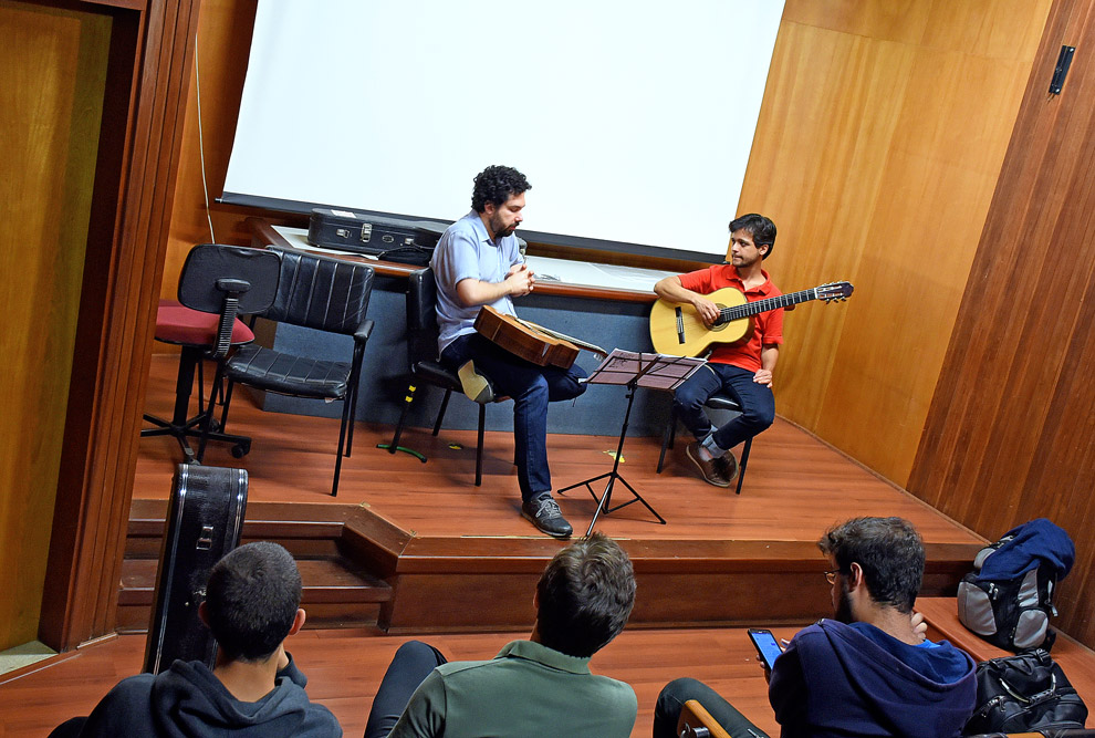 Luciano Morais no palco com um aluno, observados por mais três alunos sentados na plateia