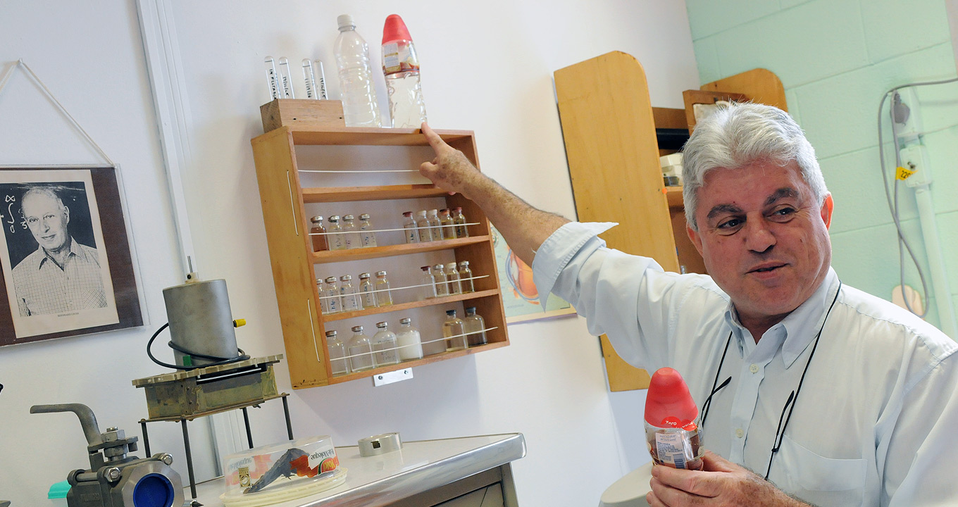 O professor João Sinézio, orientador da tese: “Muitas vezes as empresas não sabem o que a universidade está desenvolvendo” | Foto: Antoninho Perri Audiodescrição: Em laboratório, imagem frontal e de busto, homem em pé, à direita na imagem, aponta com o dedo indicador da mão direita para um frasco de plástico transparente contendo líquido incolor, erguendo o braço direito para o lado e para cima. Esse frasco, com cerca de trinta centímetros de altura, está junto a uma garrafa pet e a tubos de ensaio. Esses materiais estão dispostos sobre uma pequena estante de madeira, com cerca de sessenta centímetros de altura por sessenta de largura. Imagem 1 de 1.