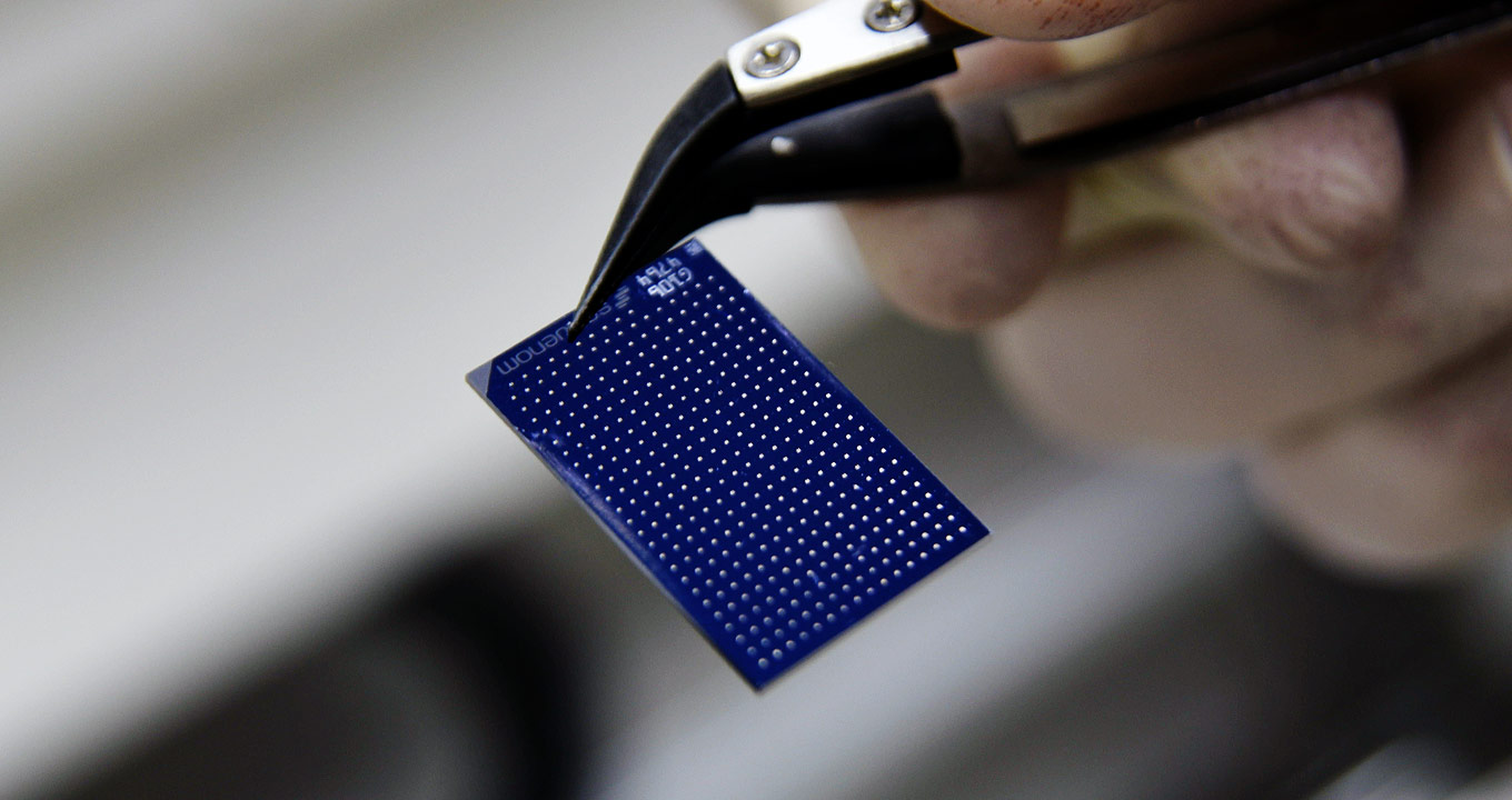 Dispositivo usado nas pesquisas | Foto: Antonio Scarpinetti Audiodescrição: Em laboratório, imagem close-up, mão direita, com luva cirúrgica, segura um tipo de pinça onde há, preso na ponta, um dispositivo com cerca de três centímetros por quatro centímetros, azul, e com vários pontinhos alinhados na vertical e na horizontal. Imagem 1 de 1.