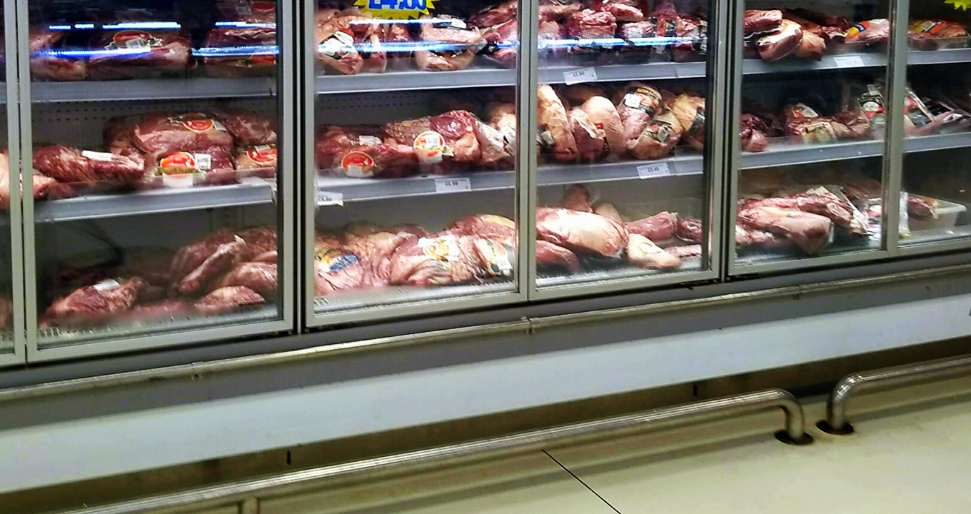 AudiodescriÃ§Ã£o: Em Ã¡rea interna de um supermercado, imagem em perfil, dezenas de pacotes de carne embalada Ã  vÃ¡cuo depositadas para venda em seis refrigeradores retangulares e com portas de vidro transparente, dispostos um ao lado do outro, sendo que as carnes estÃ£o sobre trÃªs extensas prateleiras horizontais. Imagem 1 de 1.