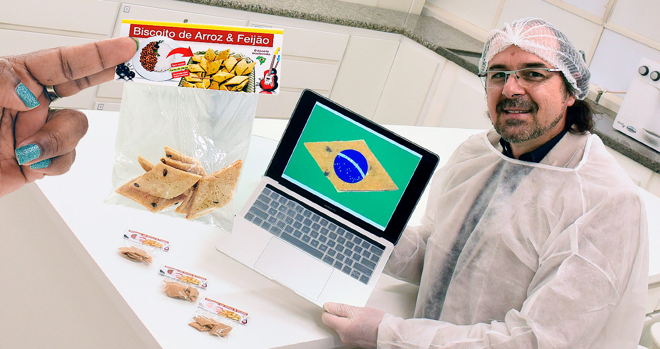 David Wesley da Silva, autor da tese; no destaque, o biscoito desenvolvido pelo pesquisador | Foto: Antoninho Perri Audiodescrição: Em laboratório, imagem em perspectiva e de busto, homem sentado em cadeira, à direita na imagem, tendo ao lado uma mesa retangular branca, onde apoia o braço direito. Às costas dele, ao fundo, em formato ele, balcão de granito cinza, com móveis brancos com gavetas e portas embutidos em toda extensão. Há um notebook aberto que mostra foto da bandeira do Brasil com um biscoito no formato losango inserido. À direita, parte de uma mão esquerda segurando saco plástico com biscoitos. Imagem 1 de 1