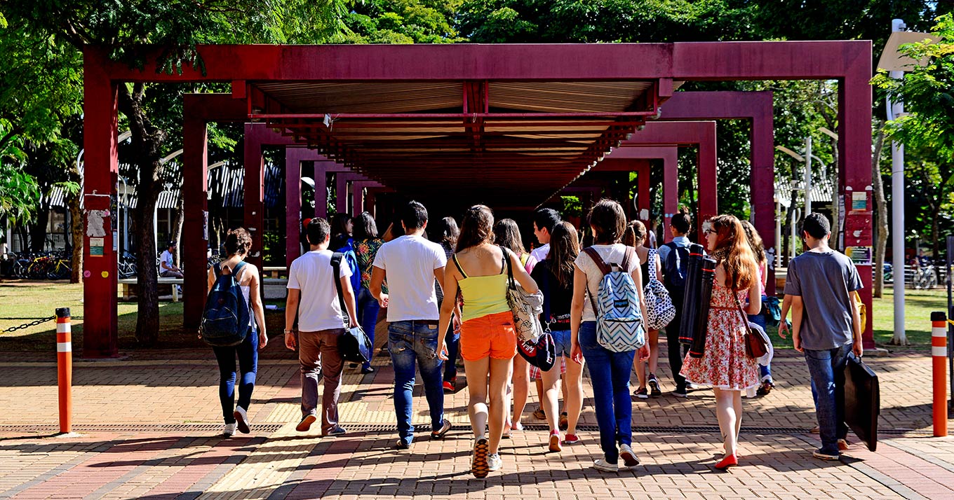 audiodescrição: fotografia colorida de estudantes caminhando pelo campus