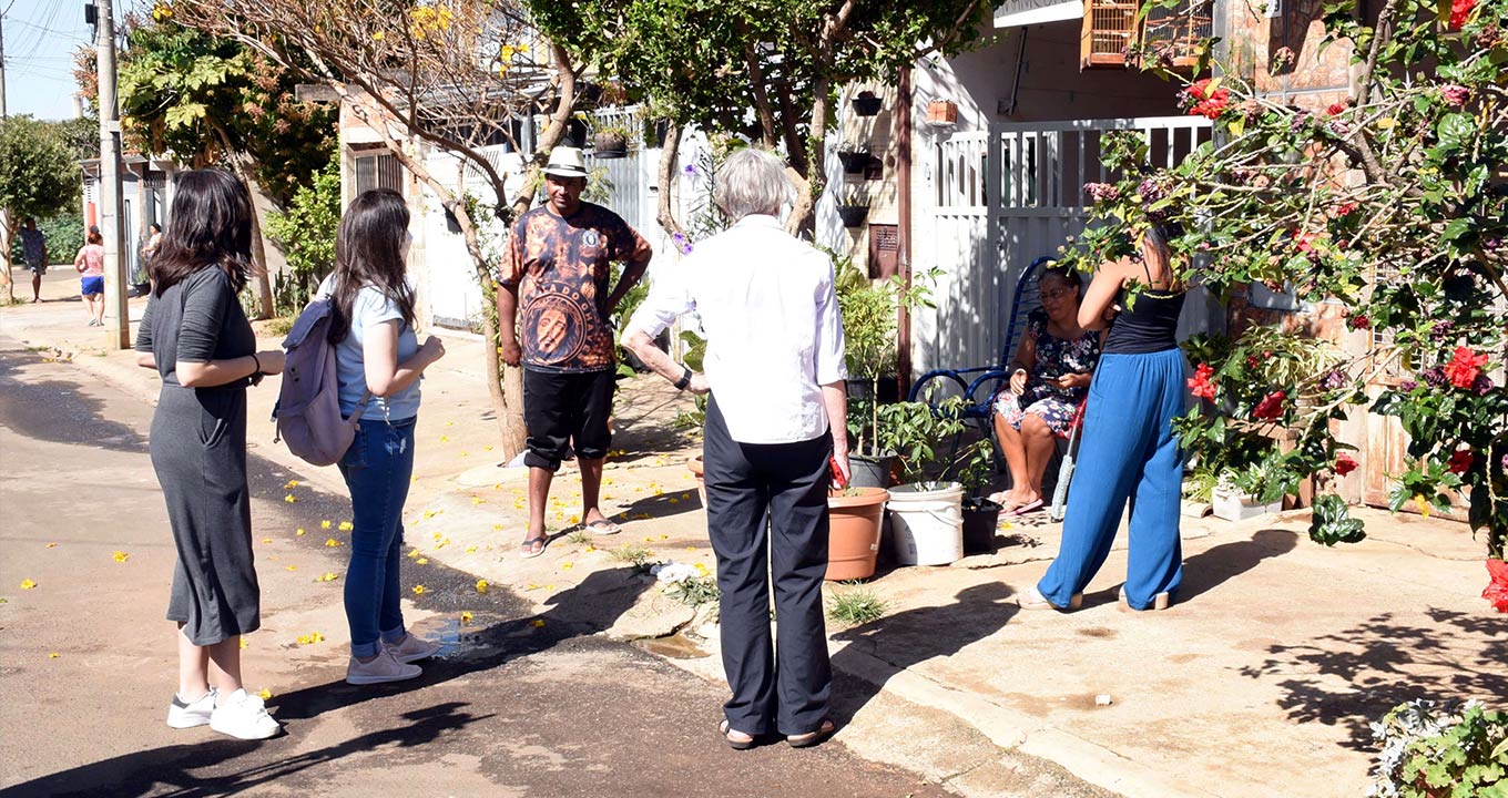 Imagem mostra grupo de pessoas conversando na rua, em frente à uma casa.