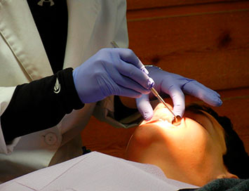 Foto mostra dentista examinando a boca de um paciente.
