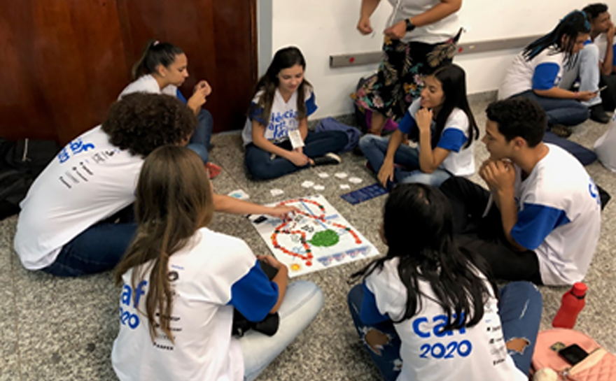 Foto de um grupo de jovens sentados no chão em torno de um jogo de tabuleiro