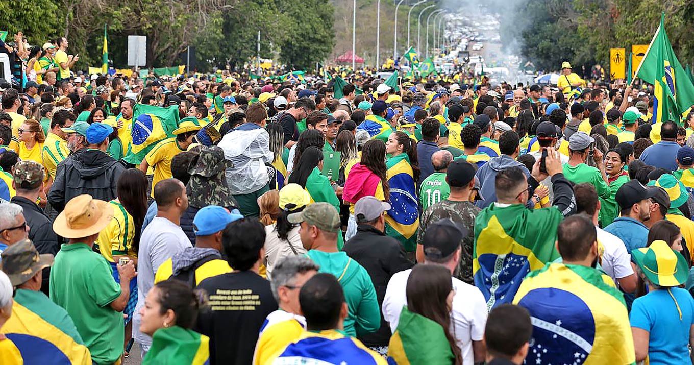 Foto de manifestantes em um espaço aberto. Eles usam camisetas nas cores verde e amarelo e seguram bandeiras do Brasil.