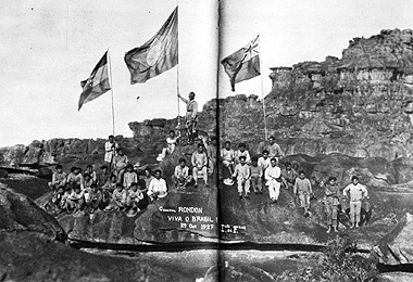 Rondon no topo do monte Roraima, na fronteira do Brasil com a Venezuela e a Guiana Inglesa, com as bandeiras dos três países, e acompanhado de índios macuxis, em 27 de outubro de 1927