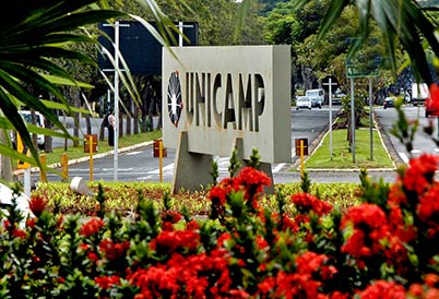 Imagem colorida, no centro da imagem está uma placa de concreto com o logo e o nome unicamp.